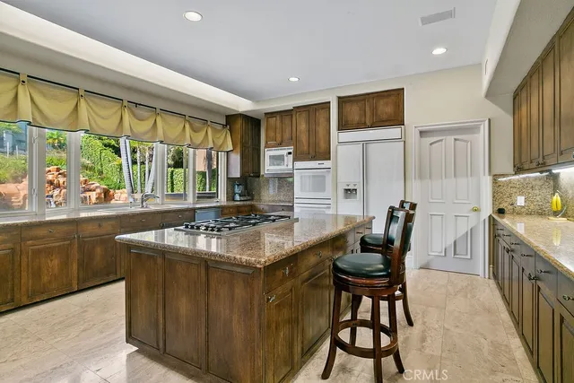 a kitchen with stainless steel appliances granite countertop a stove a refrigerator a kitchen island a sink dishwasher and white cabinets with wooden floor