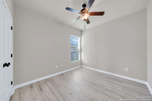 an empty room with wooden floor chandelier fan and windows