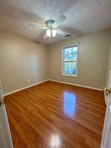 an empty room with wooden floor chandelier fan and windows