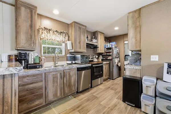 a kitchen with stainless steel appliances granite countertop a stove top oven a sink dishwasher and a refrigerator with wooden floor
