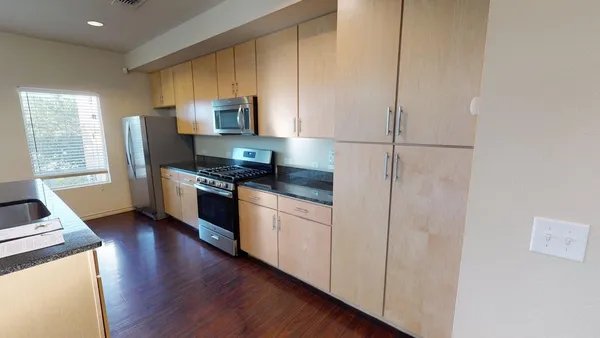 a kitchen with granite countertop stainless steel appliances a refrigerator cabinets and wooden floor