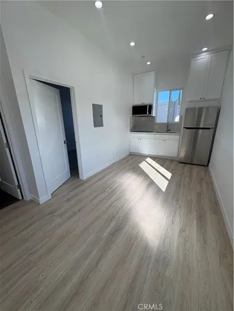 a view of empty room with wooden floor and kitchen