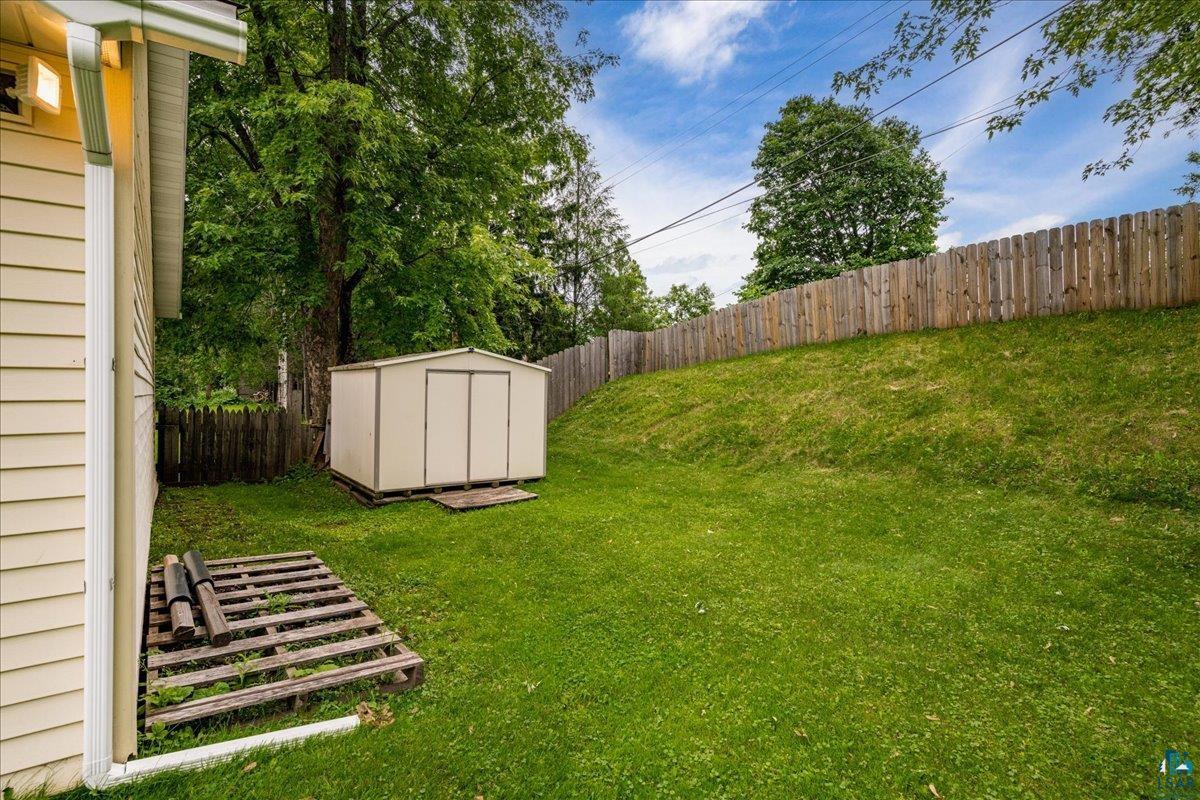 130 West Austin Street Duluth, MN 55803 - Photo 31 of 35 Expansive grassy yard featuring a storage shed with double doors, wood fencing, and mature trees