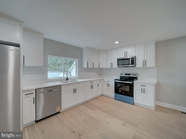 a large white kitchen with stainless steel appliances granite countertop a refrigerator and a sink