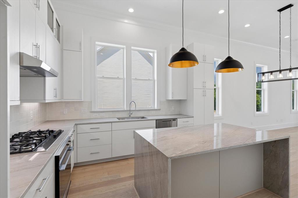 Open-concept kitchen featuring an oversized island with stone waterfall countertop, white shaker cabinetry, stainless steel appliances, and recessed lighting