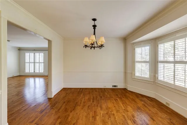 an empty room with wooden floor chandelier and windows