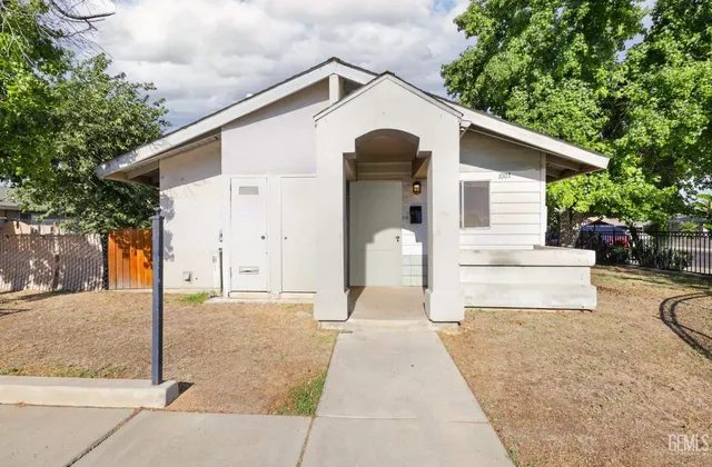 a view of a white house with a small yard plants and a large tree