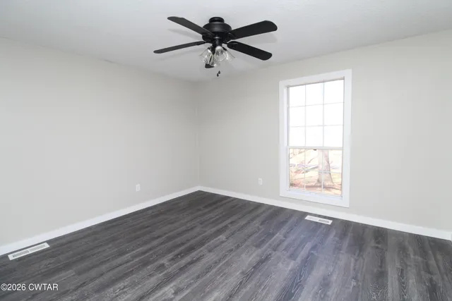 an empty room with wooden floor ceiling fan and windows
