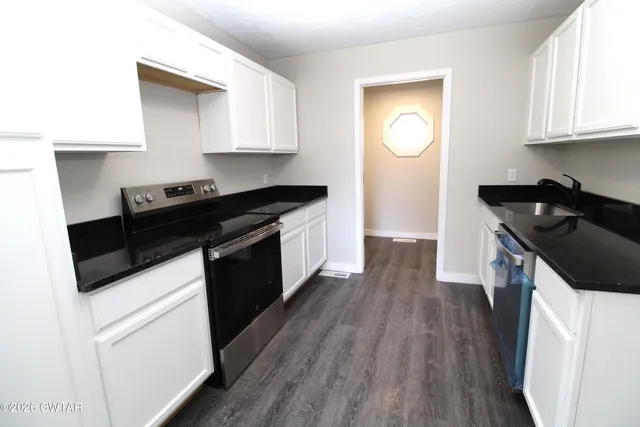 a kitchen with granite countertop stainless steel appliances a stove a sink a refrigerator wooden floor and cabinets