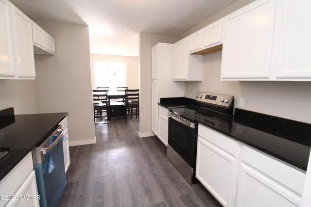 a kitchen with granite countertop a stove top oven a sink a dining table and chairs with wooden floor