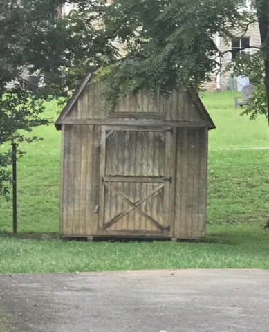 a small barn with a small yard and large trees