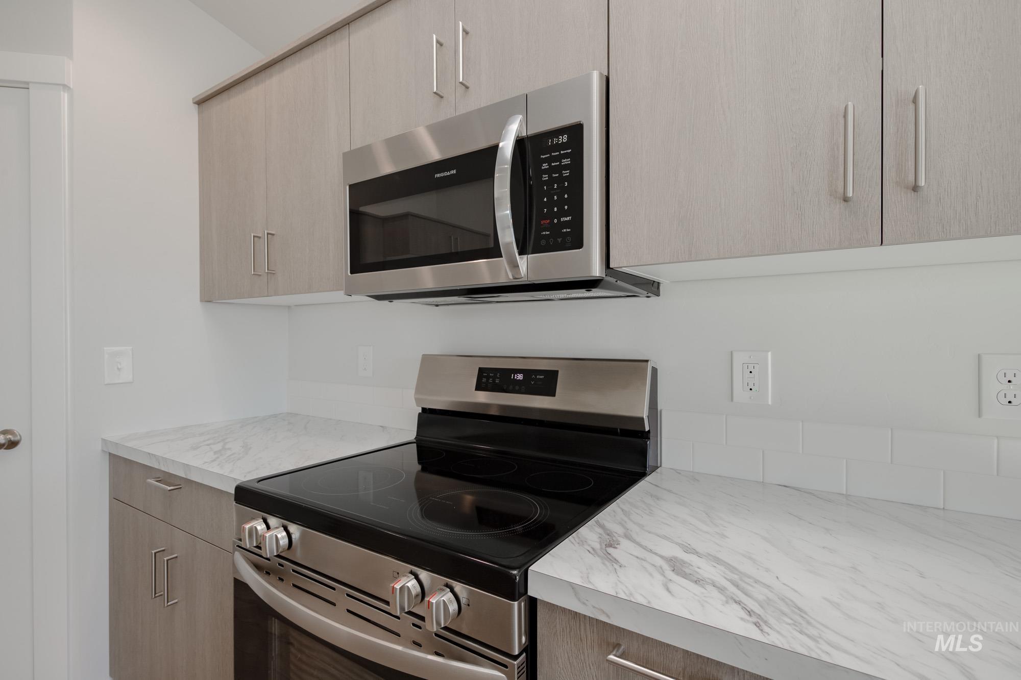 14092 Shiny Spruce Street Caldwell, ID 83607 - Photo 9 of 22 Kitchen featuring stainless steel appliances, light wood-finish cabinetry, white subway tile backsplash, and stone-look countertops