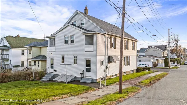 a view of a white house with a yard and table and chairs under an umbrella