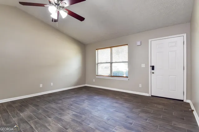 an empty room with wooden floor fan and windows