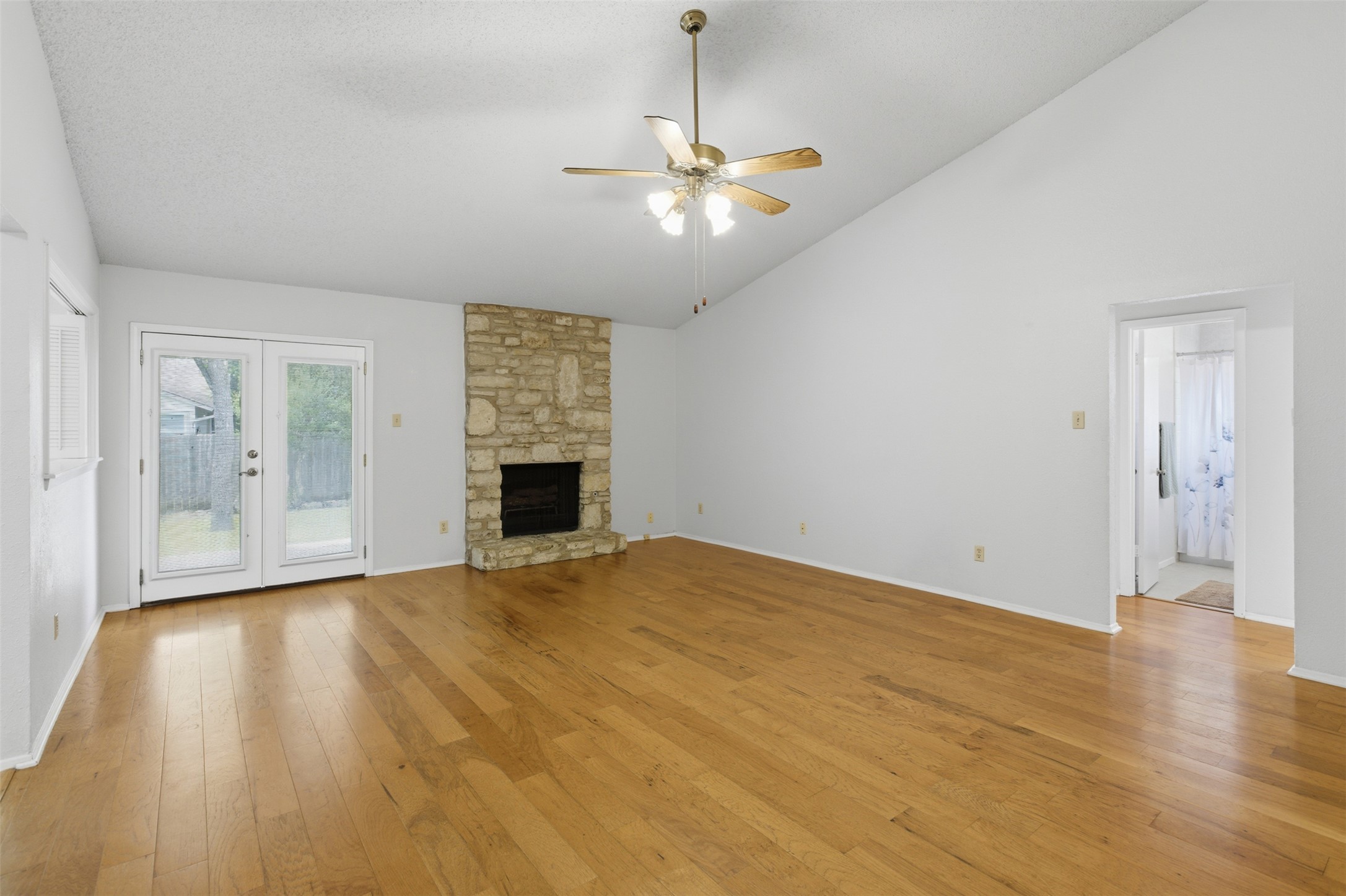 5305 Wolf Run Austin, TX 78749 - Photo 18 of 37 Expansive living area featuring vaulted ceilings, wood-finish flooring, a stone fireplace, and French doors leading to the exterior