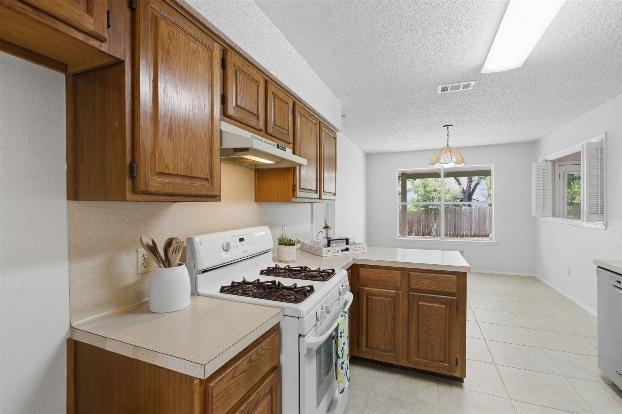 5305 Wolf Run Austin, TX 78749 - Photo 24 of 37 Kitchen featuring wood cabinetry, light-toned countertops, tile flooring, and a gas range