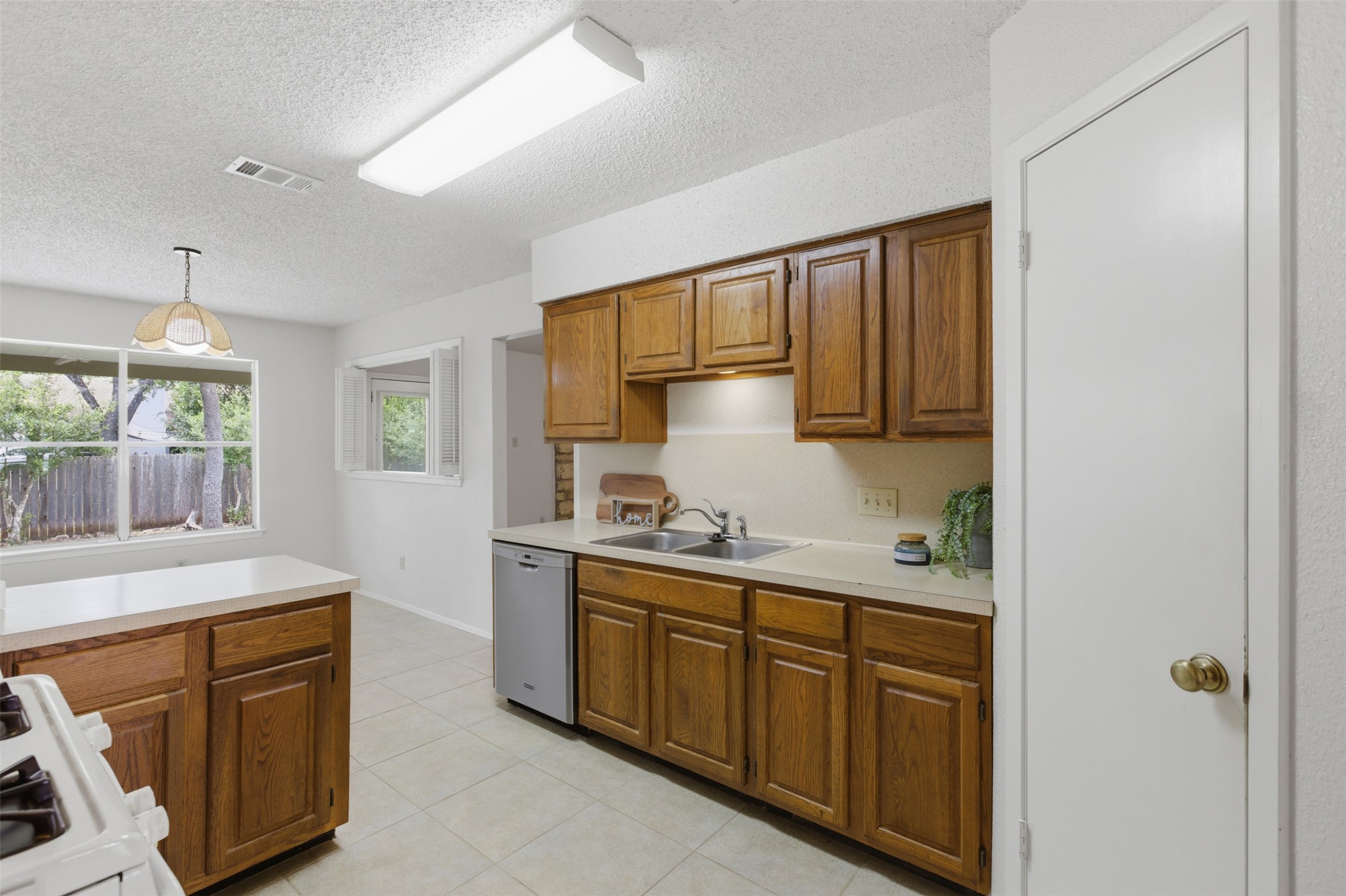 5305 Wolf Run Austin, TX 78749 - Photo 25 of 37 Kitchen featuring wood cabinetry, light-toned countertops, tile flooring, a stainless steel dishwasher, and a double basin sink