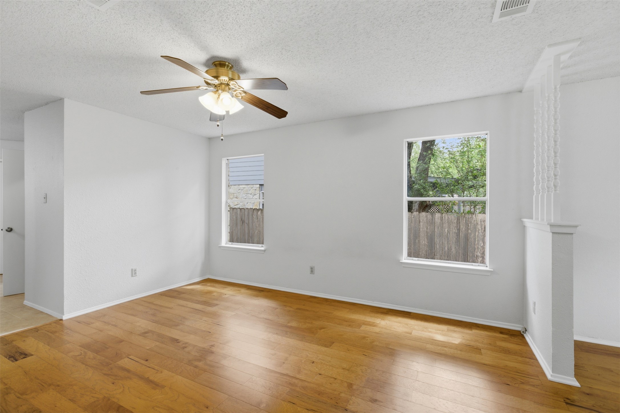5305 Wolf Run Austin, TX 78749 - Photo 33 of 37 Bright interior space featuring wood-finish flooring, two windows, a ceiling fan with light fixture, and a partial balustrade