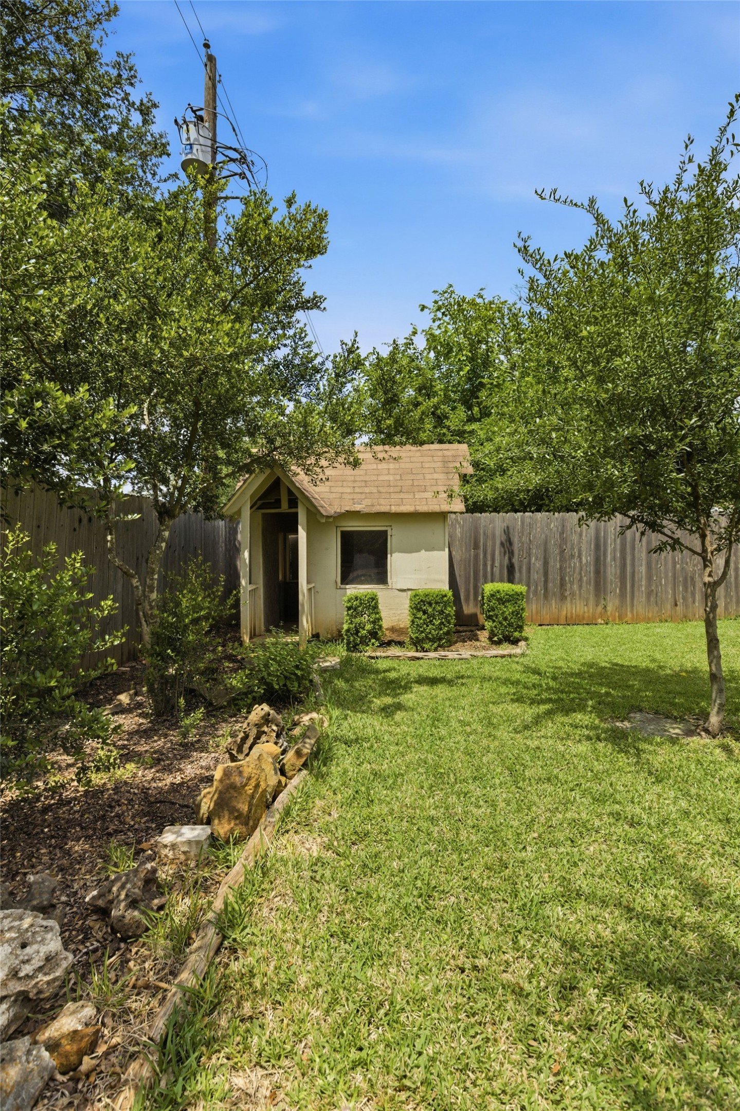 5305 Wolf Run Austin, TX 78749 - Photo 36 of 37 Expansive backyard featuring a lush lawn, mature trees, wood fence, and a storage shed with a shingled roof