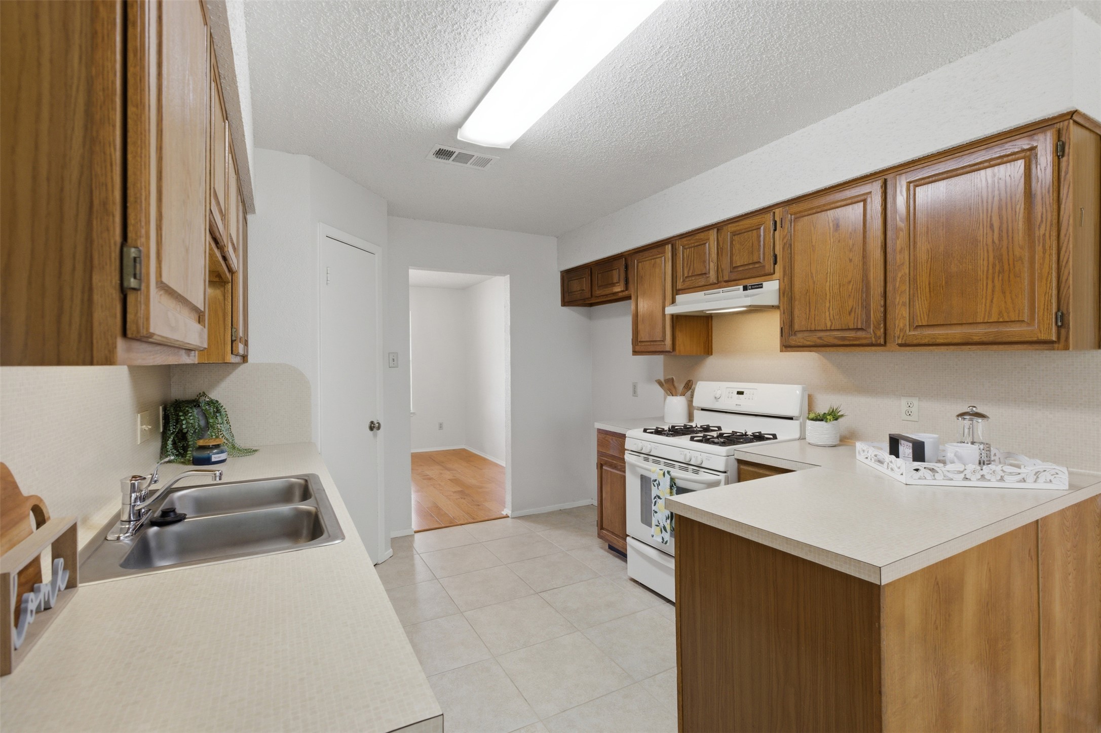 5305 Wolf Run Austin, TX 78749 - Photo 6 of 37 Kitchen featuring warm wood cabinetry, neutral countertops, a double basin stainless steel sink, white gas range with a matching range hood, and tile flooring