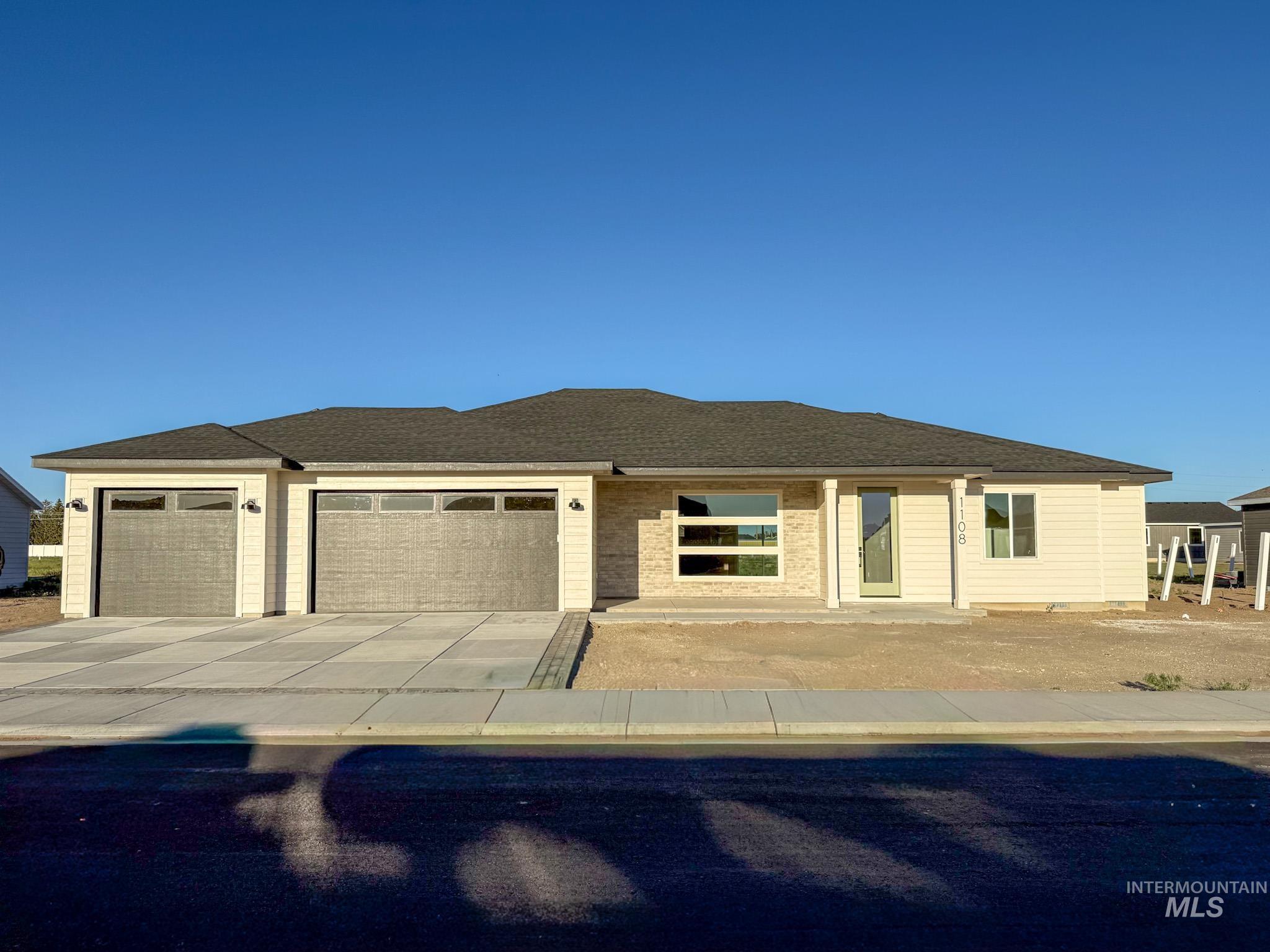 1108 Sage Rupert, ID 83350 - Photo 1 of 21 Modern ranch-style exterior featuring a multi-pane window, brick façade accents, a two-car garage with textured doors, and a covered entry