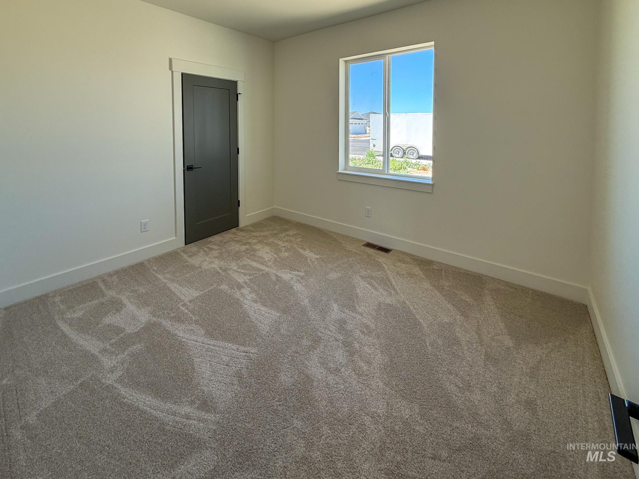 1108 Sage Rupert, ID 83350 - Photo 13 of 21 Light-filled room featuring neutral-toned walls, a single window with white trim, a dark panel door with black hardware, and plush patterned carpeting