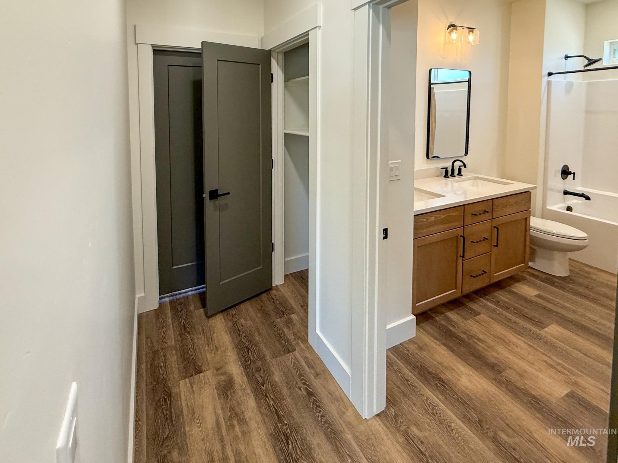 1108 Sage Rupert, ID 83350 - Photo 16 of 21 Bathroom featuring wood-finish flooring, a vanity with a white countertop and wood-tone cabinetry, a rectangular mirror, and a bathtub with a shower