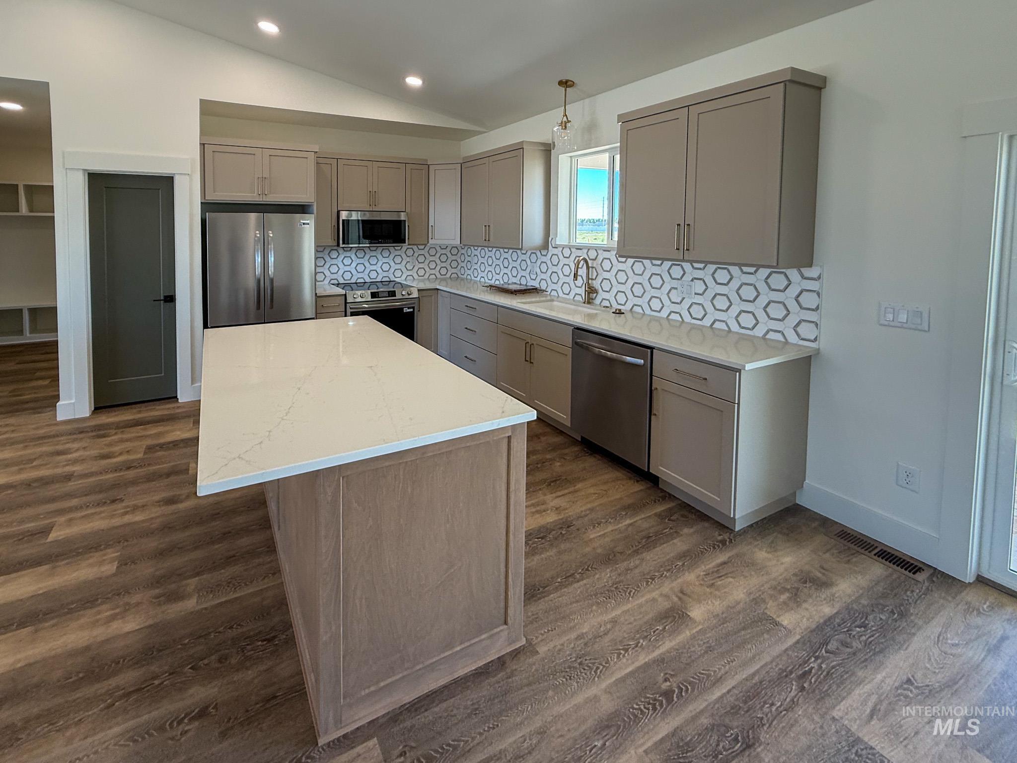 1108 Sage Rupert, ID 83350 - Photo 5 of 21 Modern kitchen featuring a large center island with a light-toned countertop, stainless steel appliances, contemporary cabinetry, a patterned tile backsplash, and wood-finish flooring