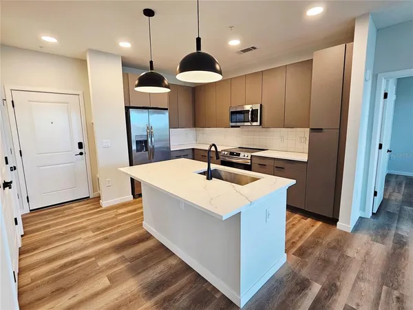 a kitchen with stainless steel appliances granite countertop a sink a microwave oven a refrigerator and white cabinets with wooden floor