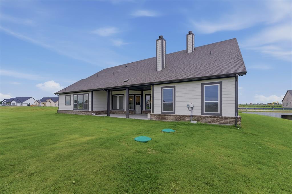 2316 Quartz Street Krum, TX 76249 - Photo 25 of 29 Rear exterior featuring an expansive green lawn, covered patio, multiple windows, and two prominent chimneys