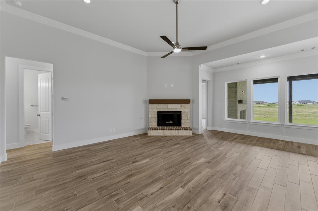 2316 Quartz Street Krum, TX 76249 - Photo 7 of 29 Spacious living area featuring wood-finish flooring, a corner fireplace with a stone surround and wood mantel, crown molding, and recessed lighting
