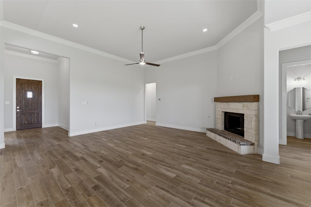 2316 Quartz Street Krum, TX 76249 - Photo 10 of 29 Spacious living area featuring wood-finish flooring, a corner fireplace with a stone surround and wood mantel, crown molding, and a ceiling fan