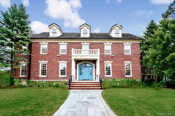 a view of a brick house with a yard potted plants and a large tree