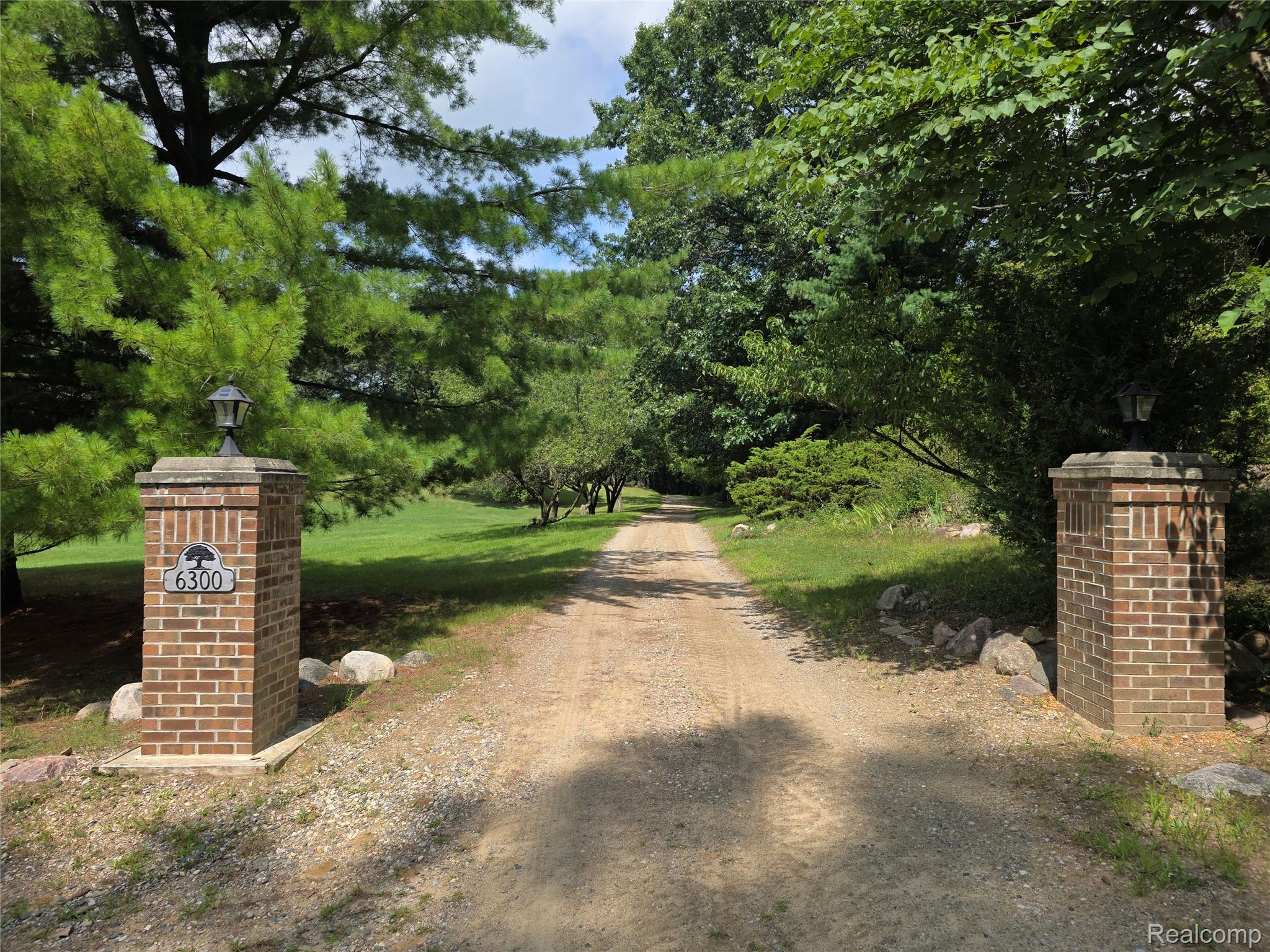 6300 North Raddatz Road Fowlerville, MI 48836 - Photo 2 of 42 Brick entry pillars with integrated lighting and house numbers, gravel drive, and mature trees