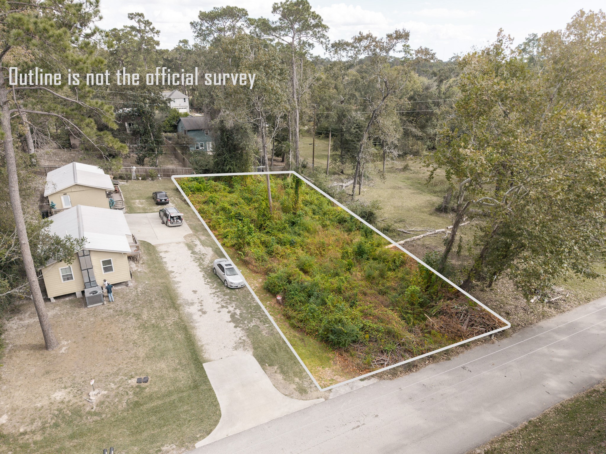 This photo shows a rectangular, overgrown lot bordered by trees, next to a small house with a driveway. The lot is outlined for reference, but note that the outline is not an official survey. It's located in a wooded residential area.