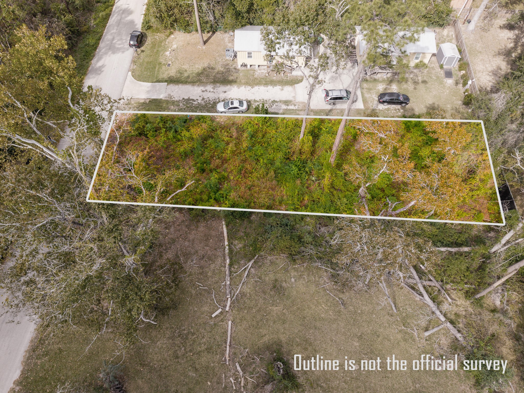 22030 Rustic Bridge Lane Houston, TX 77339 - Photo 4 of 7 This aerial photo shows a rectangular plot of land outlined in white, covered with dense vegetation and some trees. It's located adjacent to a residential street with a few houses and parked cars nearby. Note that the outline is not an official survey.