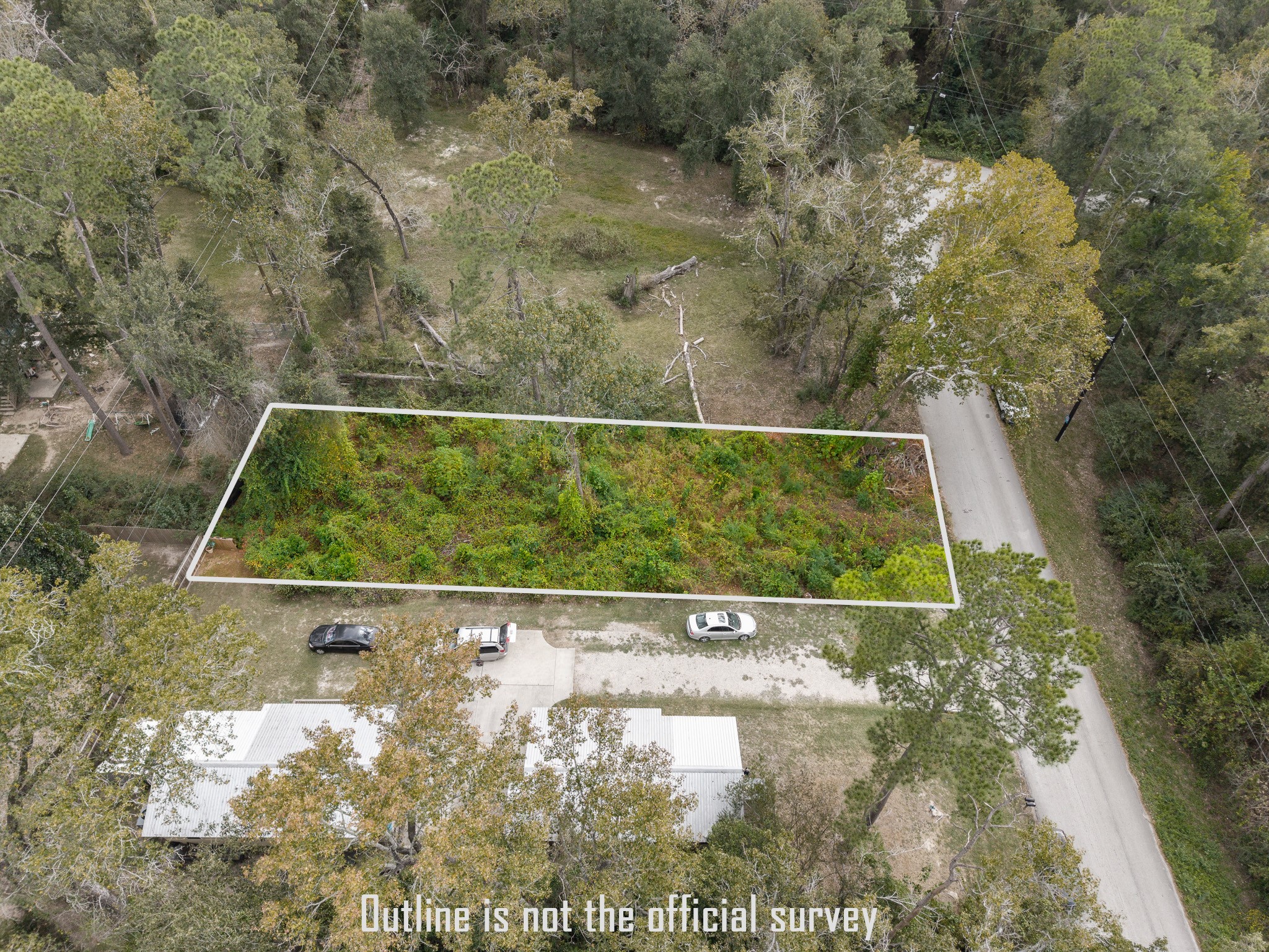 22030 Rustic Bridge Lane Houston, TX 77339 - Photo 6 of 7 This photo shows a rectangular plot of land outlined in white, located in a wooded area next to a road. The plot is densely covered with greenery, and there are a few vehicles parked nearby. Surrounding the plot are mature trees, providing a natural, secluded setting.