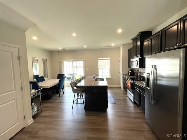 a large open kitchen with a refrigerator a stove a sink and a dining table with wooden floor