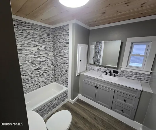 a bathroom with a granite countertop sink toilet mirror and bathtub