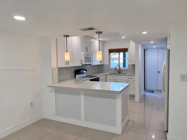 a kitchen with kitchen island white cabinets appliances a sink and a window