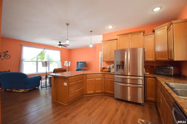 a kitchen with stainless steel appliances granite countertop a refrigerator a sink dishwasher a stove and a dining table with wooden floor