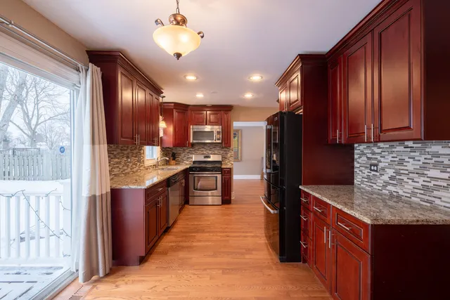 a kitchen with kitchen island granite countertop wooden cabinets a sink dishwasher stove and refrigerator with wooden floor