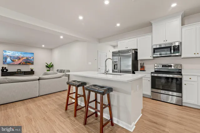 a kitchen with stainless steel appliances a stove a sink a microwave a refrigerator and white cabinets with wooden floor