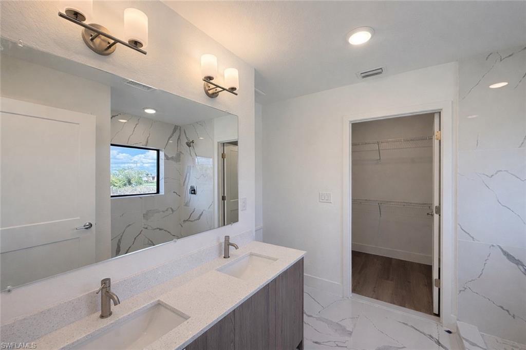 108 Indiana Place Lehigh Acres, FL 33936 - Photo 9 of 19 Full bath with light marble finish floors, a marble finish shower, double vanity, and a walk in closet