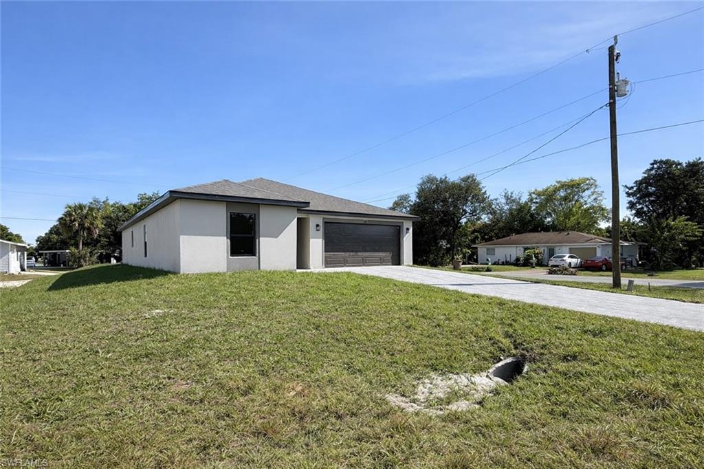 108 Indiana Place Lehigh Acres, FL 33936 - Photo 16 of 19 View of front of property with driveway, a front lawn, a garage, and stucco siding
