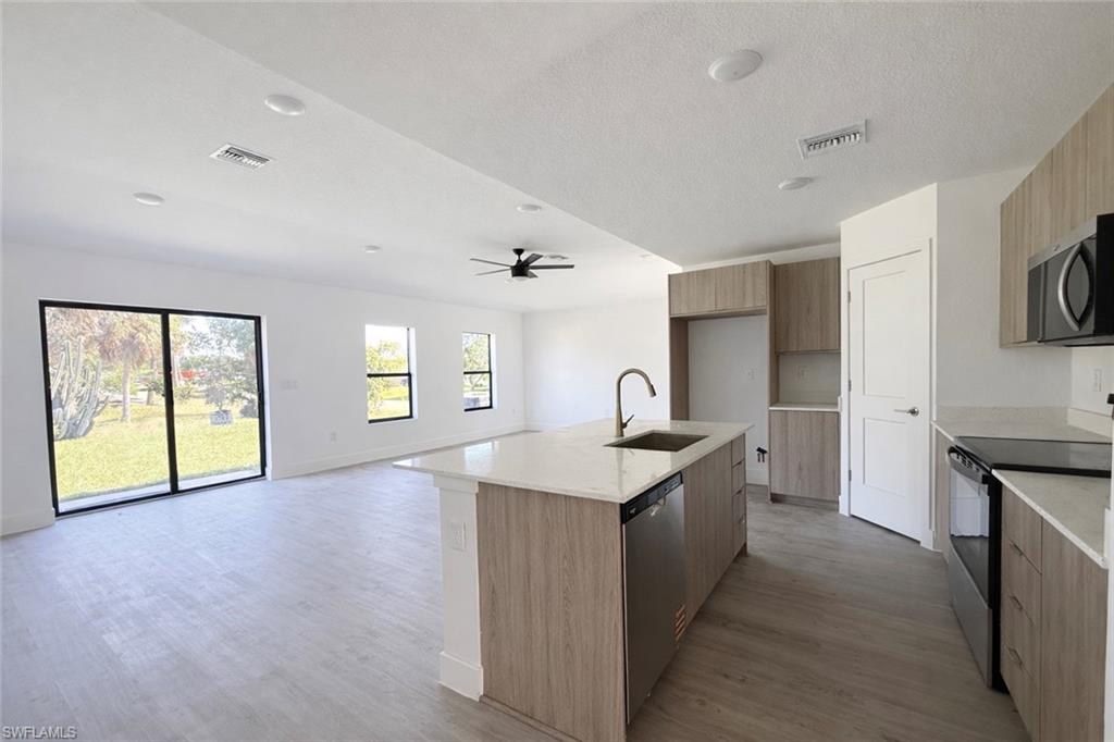 108 Indiana Place Lehigh Acres, FL 33936 - Photo 4 of 19 Kitchen featuring stainless steel appliances, light stone countertops, modern cabinets, a kitchen island with sink, and a textured ceiling