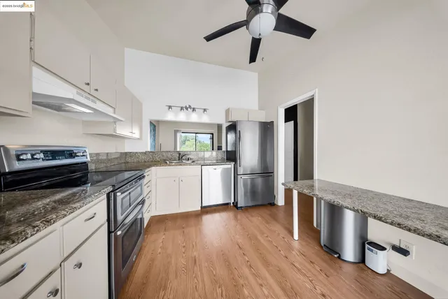 a kitchen with stainless steel appliances granite countertop a refrigerator a sink dishwasher a stove and white countertops with wooden floor