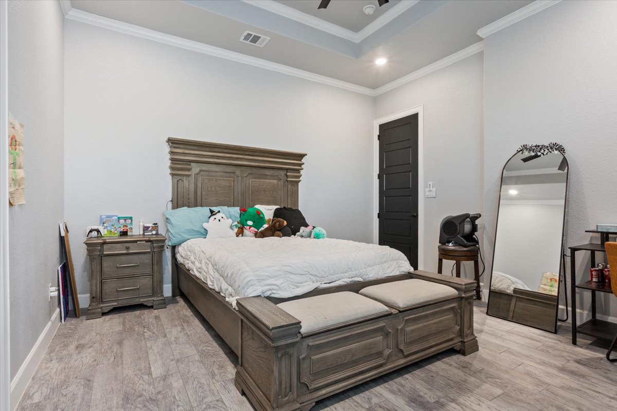 10940 Wedel Cemetery Road Rogers, TX 76569 - Photo 11 of 31 A tranquil bedroom featuring an ornate wooden bed frame, a coffered ceiling, and rich wood flooring.