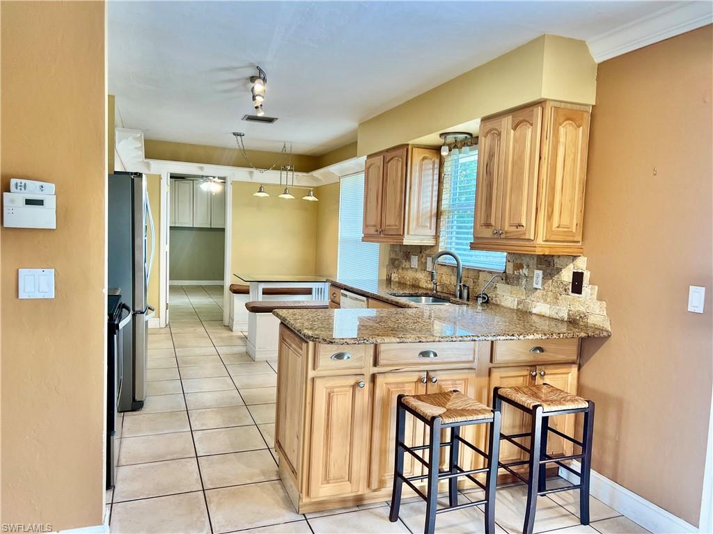 18581 Tampa Road Fort Myers, FL 33967 - Photo 4 of 25 Kitchen featuring a kitchen bar, sink, tasteful backsplash, light stone counters, and kitchen peninsula