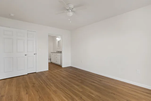 a view of an empty room with wooden floor and a ceiling fan
